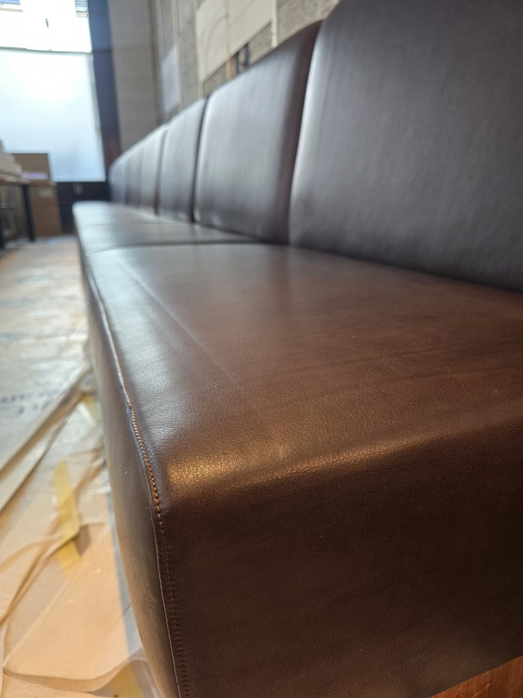 Close view along a brown upholstered bench, showing the seat edge and stitching.
