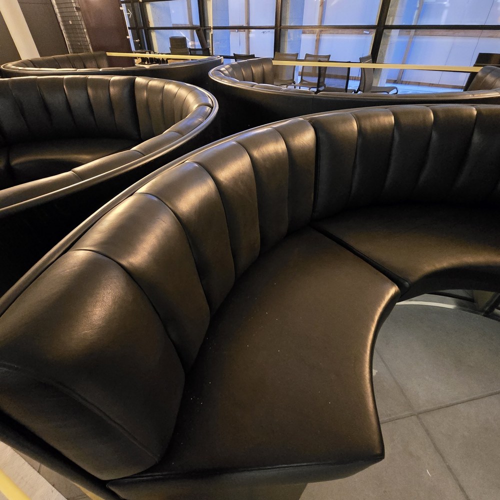Close view of a curved dark upholstered bench with vertical divisions in its padded back.